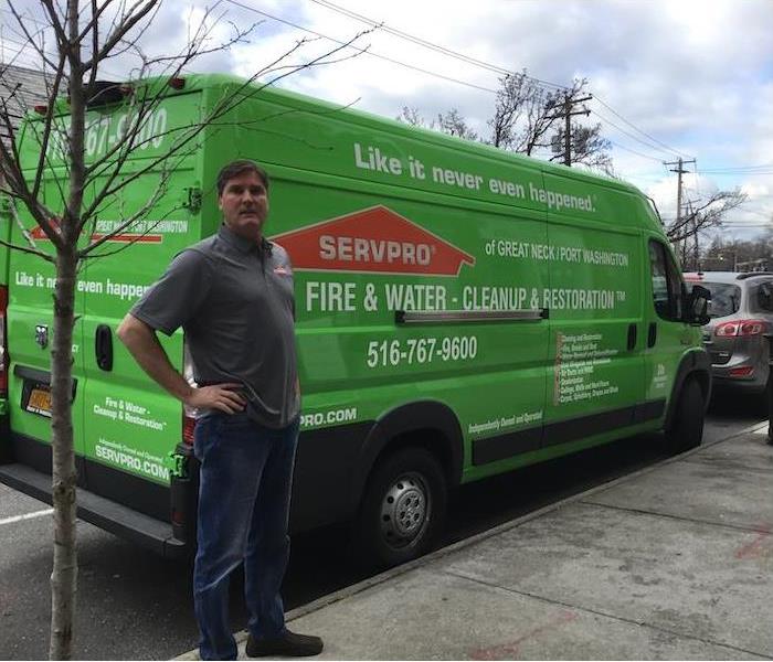 SERVPRO van parked on the street with a male employee posing at the back